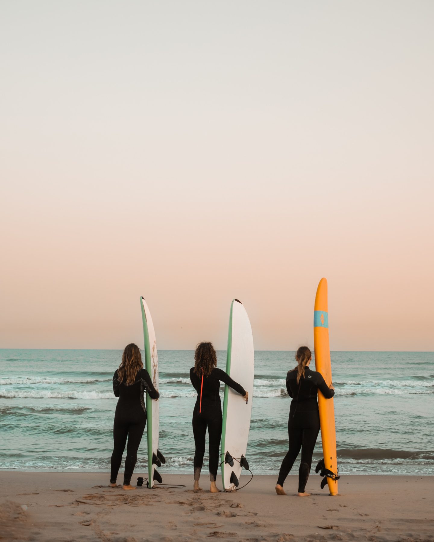 Drie surfers met surfboard op een rij, kijkend naar de zee.