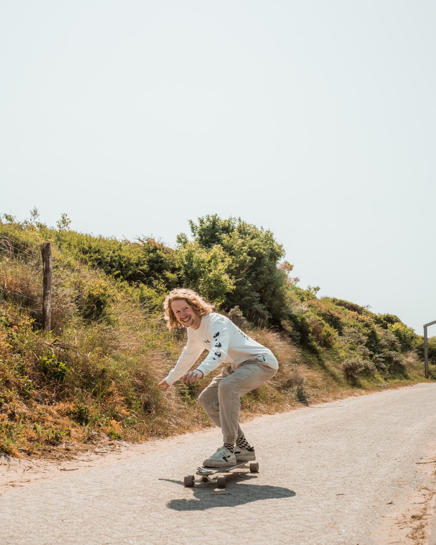 Man op een longboard in de duinen.