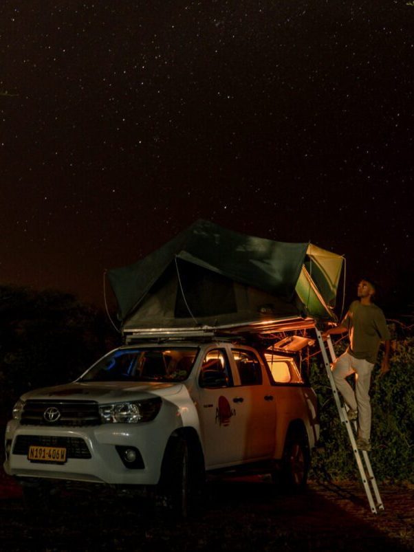 Een persoon bij een auto met daktent in het donker in Namibië tijdens Namibia Nomads.