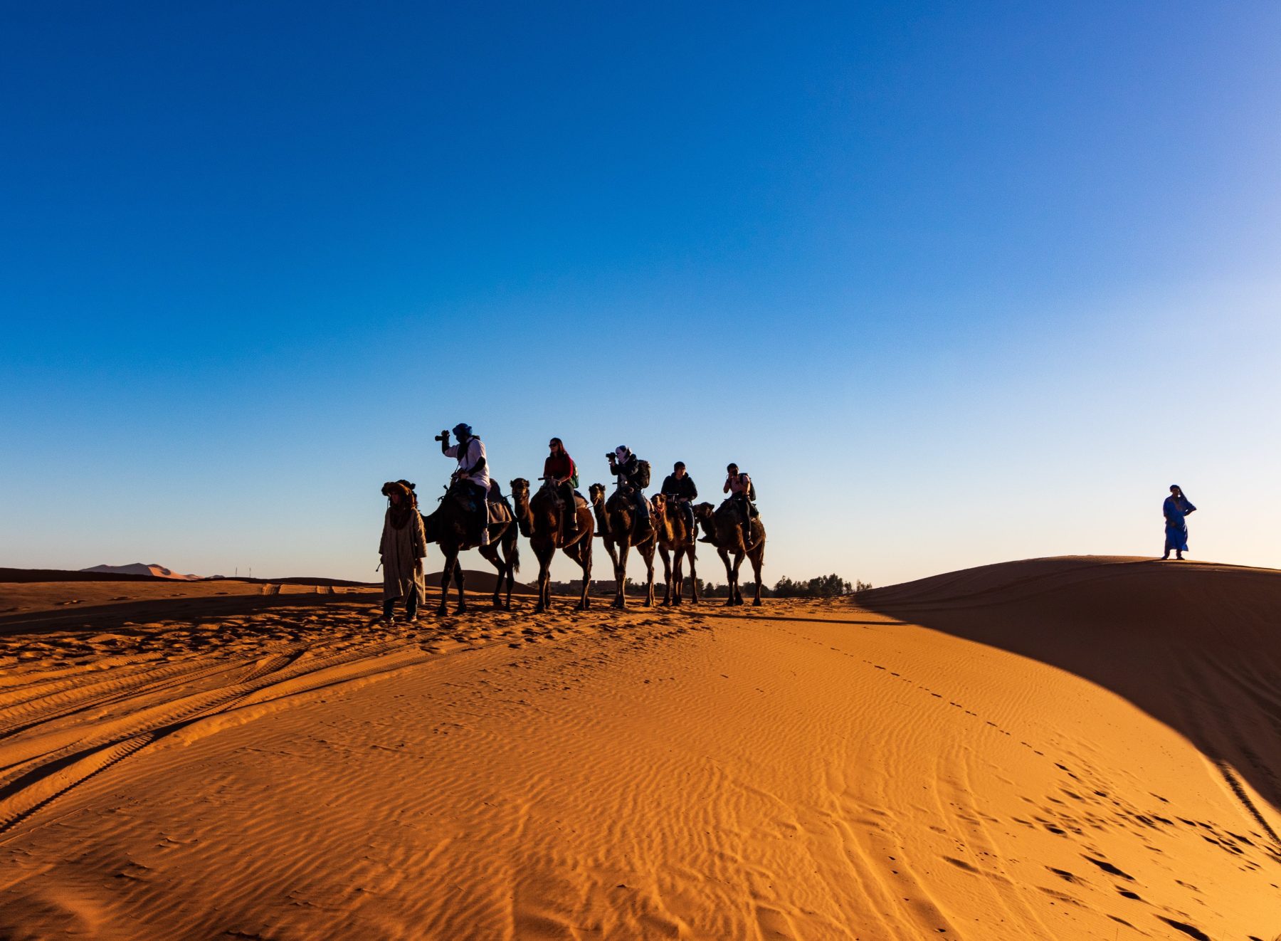 Mensen en kamelen trekkend door de woestijn in Marokko.
