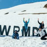 Mensen staan op een besneeuwde berg rondom grote letters waarmee '#WPMDAYS' is gespeld.