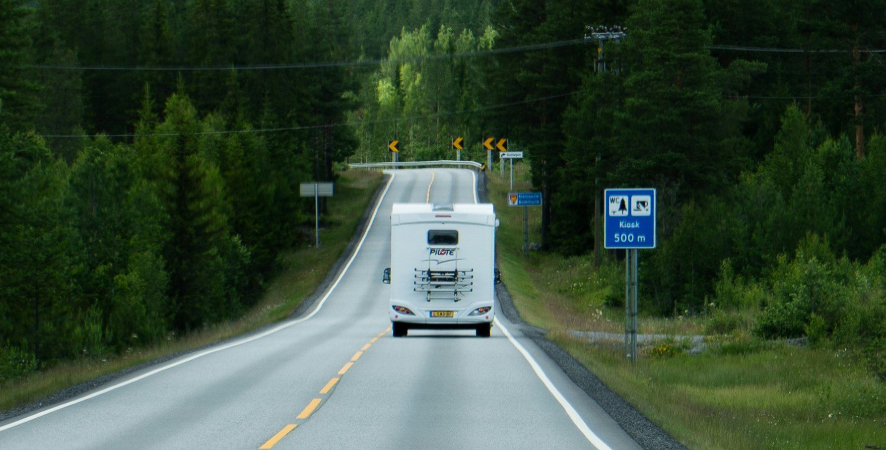 Een camper rijdend over een weg in Scandinavië met op de achtergrond bossen.