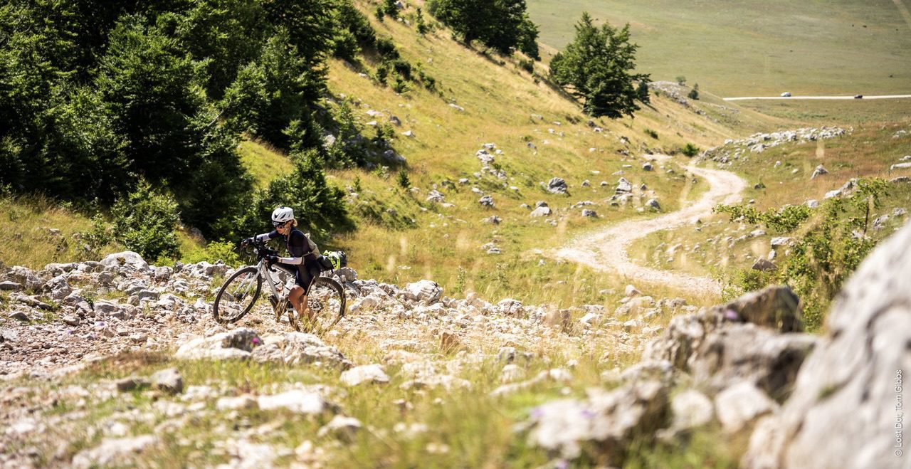 Een vrouw loopt met haar fiets in de hand door een rotsachtig landschap.