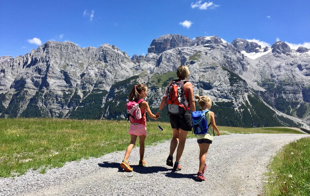 Een vrouw loopt tijdens een zonnige dag met twee kinderen door de Dolomieten.