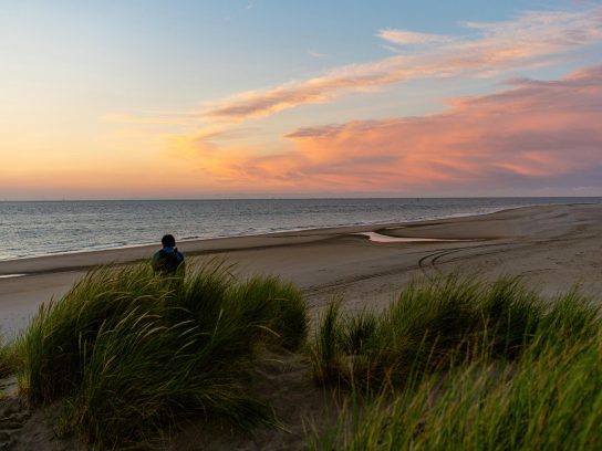 Een persoon zit op het strand tijdens zonsondergang.