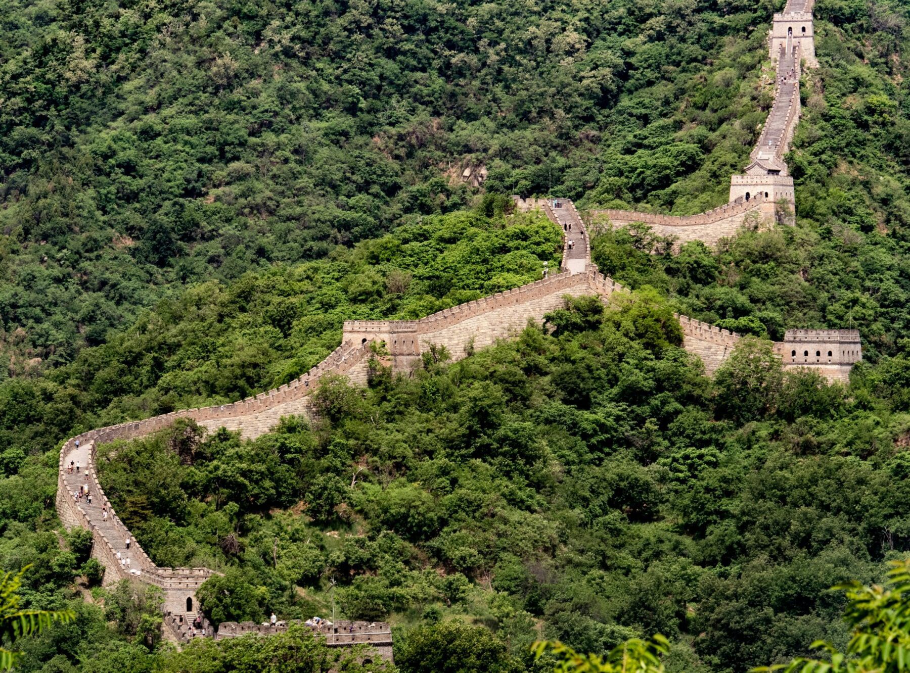 De Chinese Muur kronkelend door een bebost berglandschap.