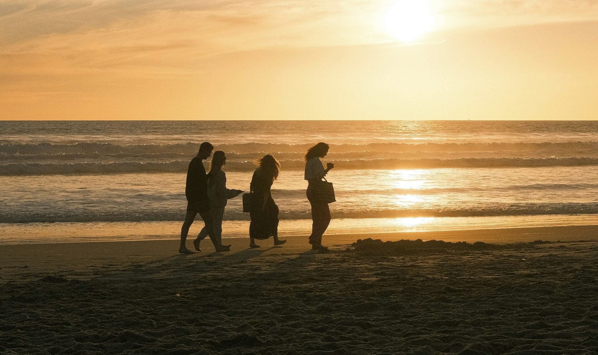 Vier personen wandelend langs de kustlijn tijdens zonsondergang.